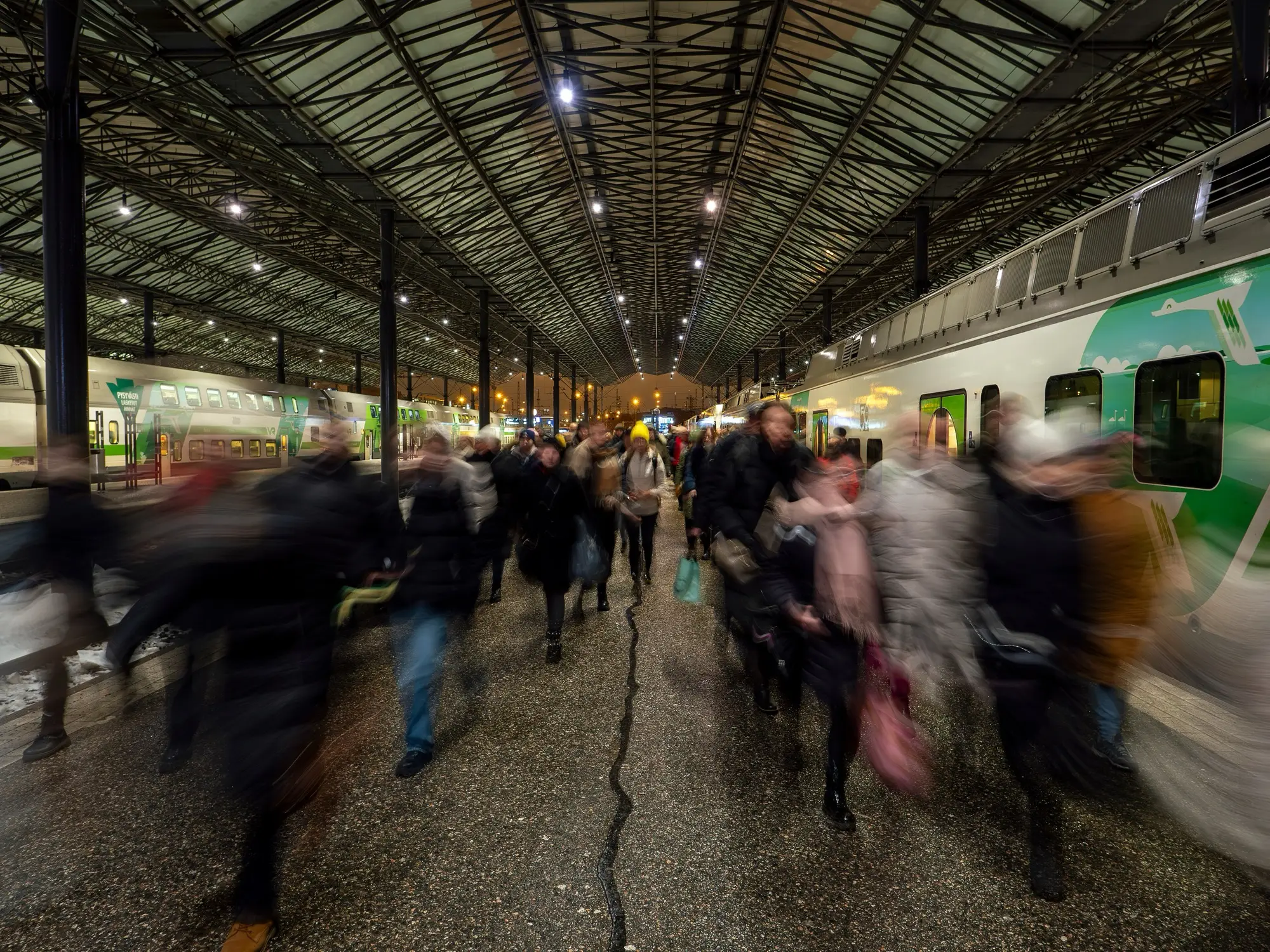 Commuters streaming along a platform under the canopy of Helsinki Central railway station during the morning rush, beside a green-and-white train.