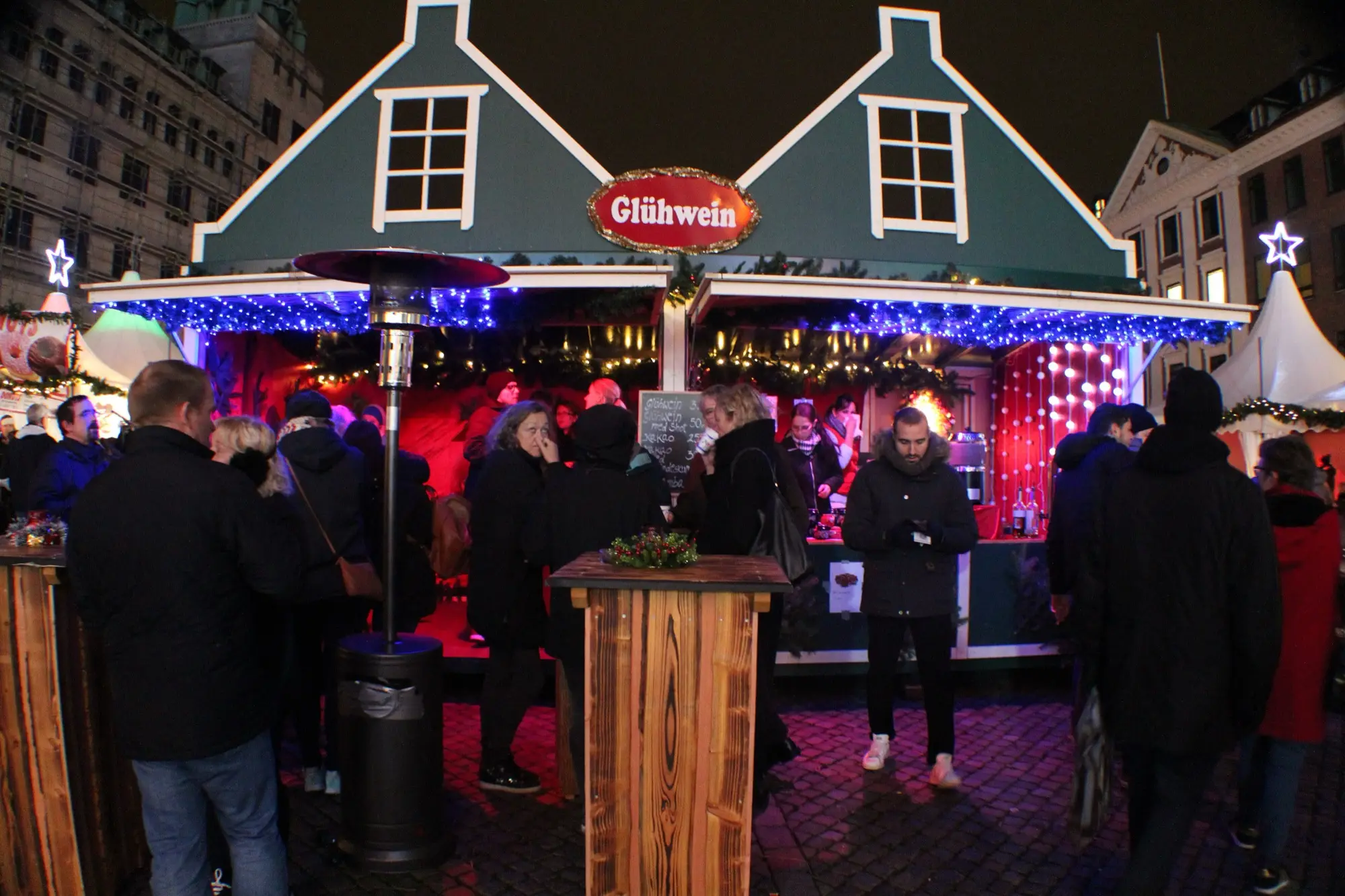 A Glühwein stall at the Christmas market on Nytorv in Copenhagen, lit up at night with people standing at tall tables