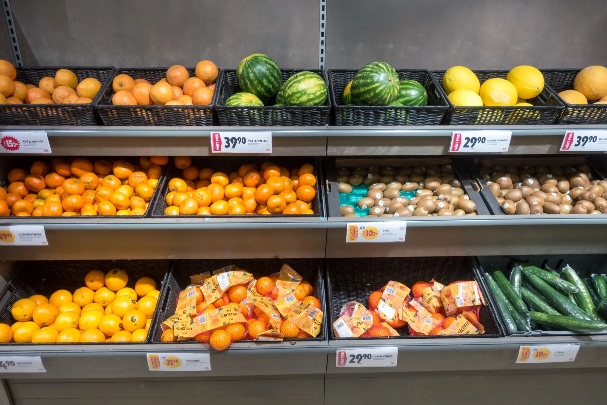 Shelves of oranges, melons, lemons, kiwis and cucumbers in a Stockholm grocery store, with price tags in Swedish kronor.