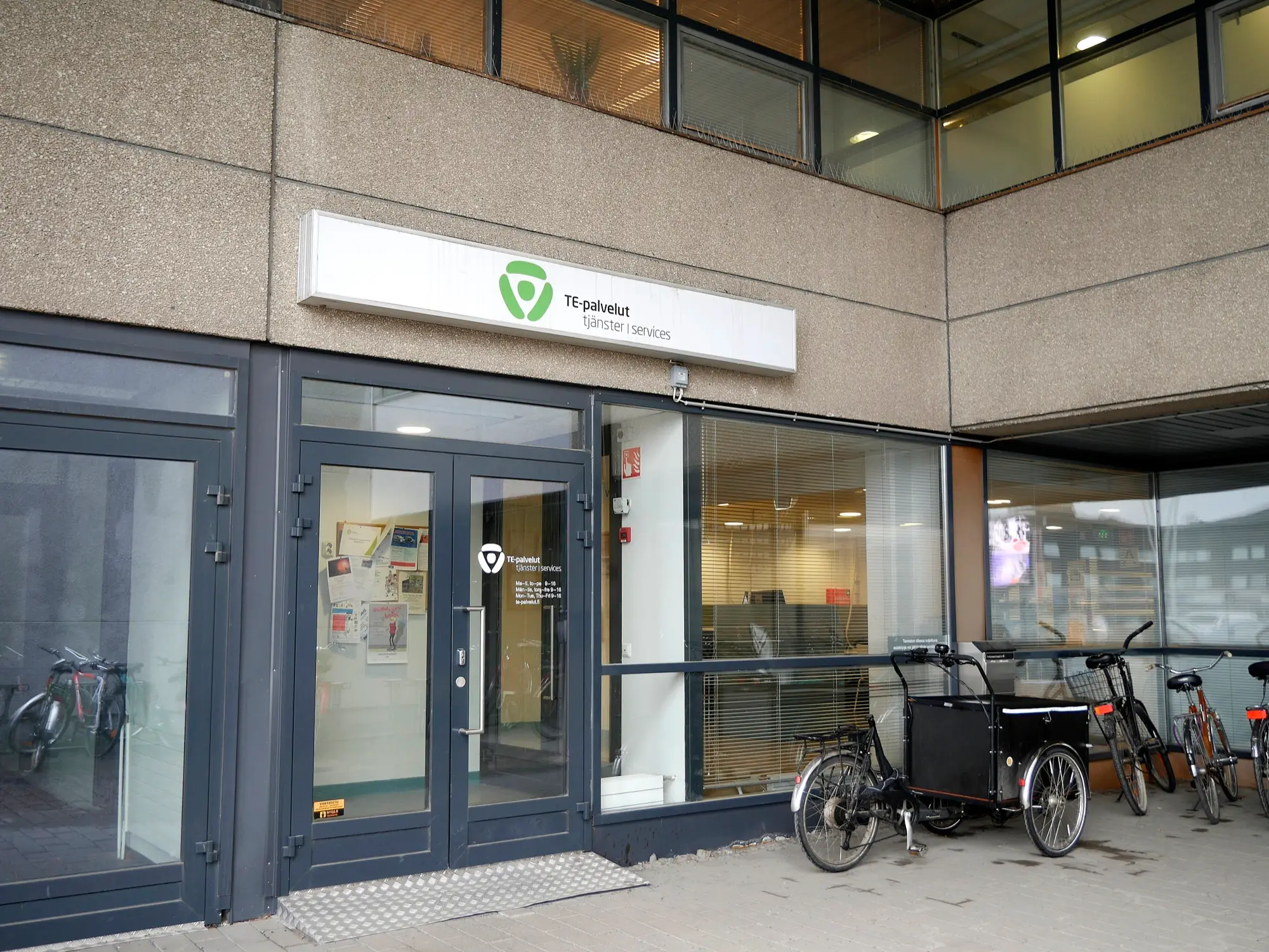 The glass entrance of a TE office in Seinäjoki with the green TE-palvelut sign above the door and bicycles parked outside.