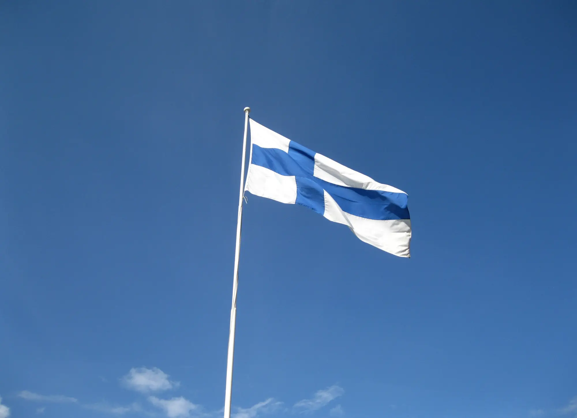 The blue-cross flag of Finland flying from a flagpole against a clear blue sky.