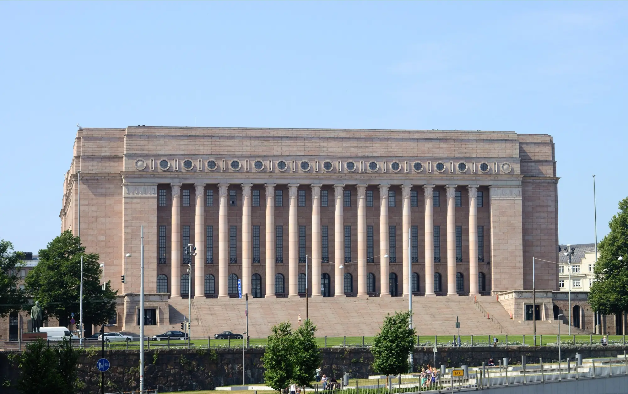The colonnaded granite facade of Parliament House in Helsinki on a clear summer day.