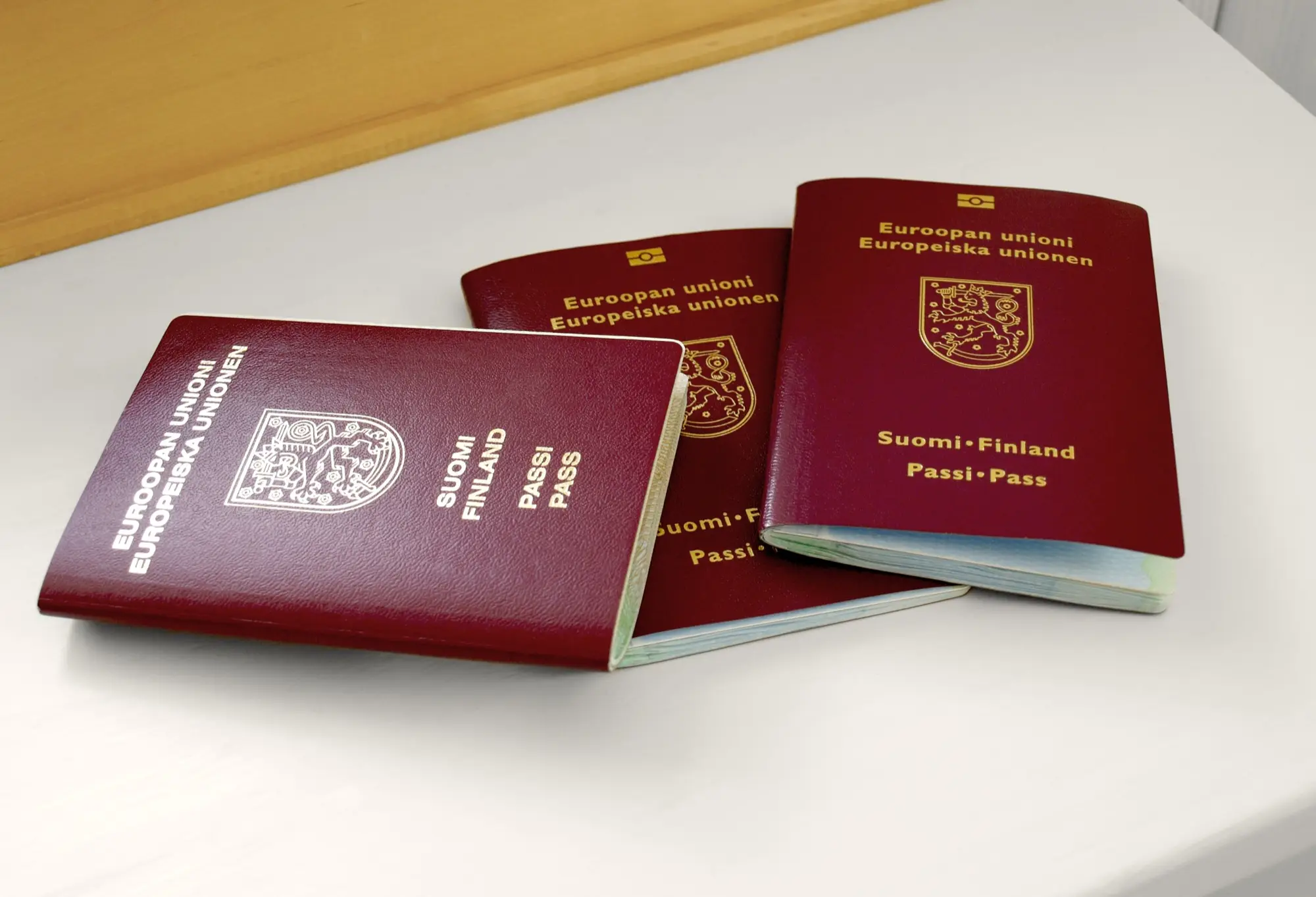 Three burgundy Finnish passports with the gold lion coat of arms lying on a white table.