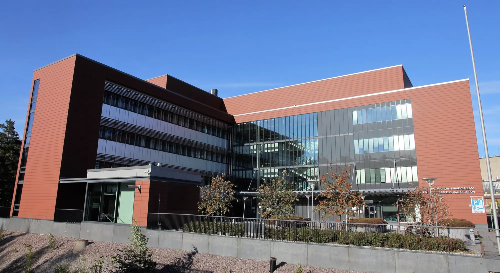 The red-brick and glass Myllypuro health station in Helsinki under a blue sky.