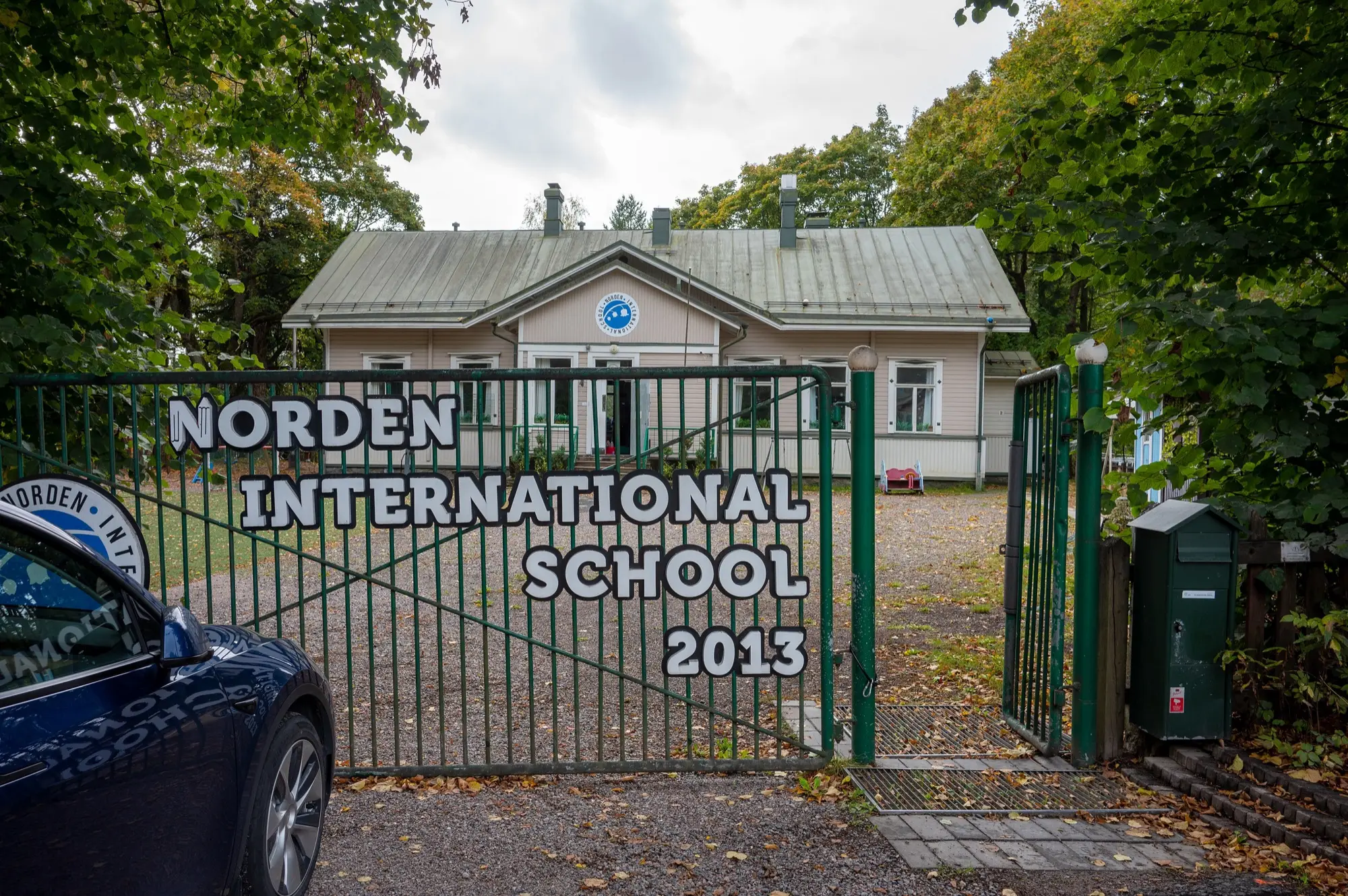 A green gate with a Norden International School sign in front of a small school building in Malmi, Helsinki.
