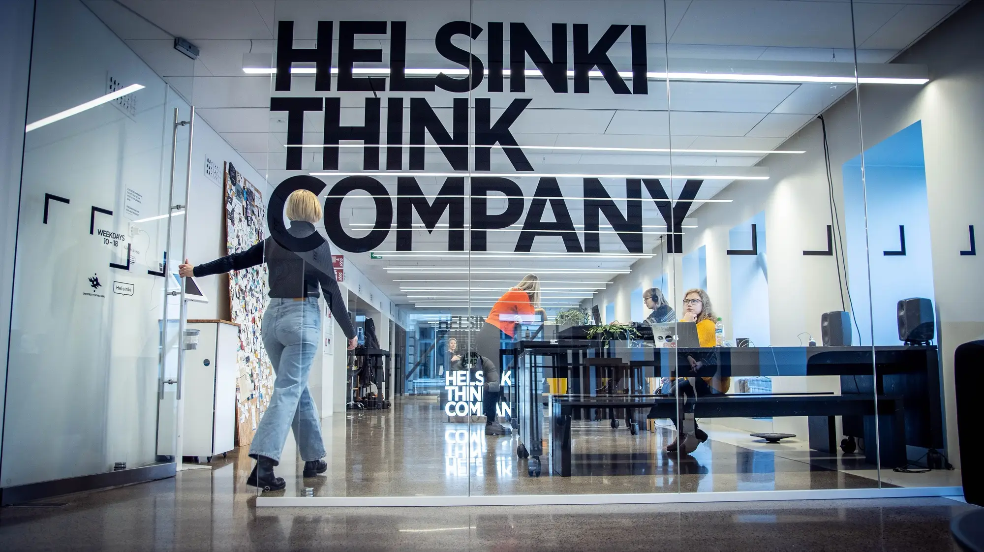A coworking space behind a glass wall lettered Helsinki Think Company, with people working at desks inside.
