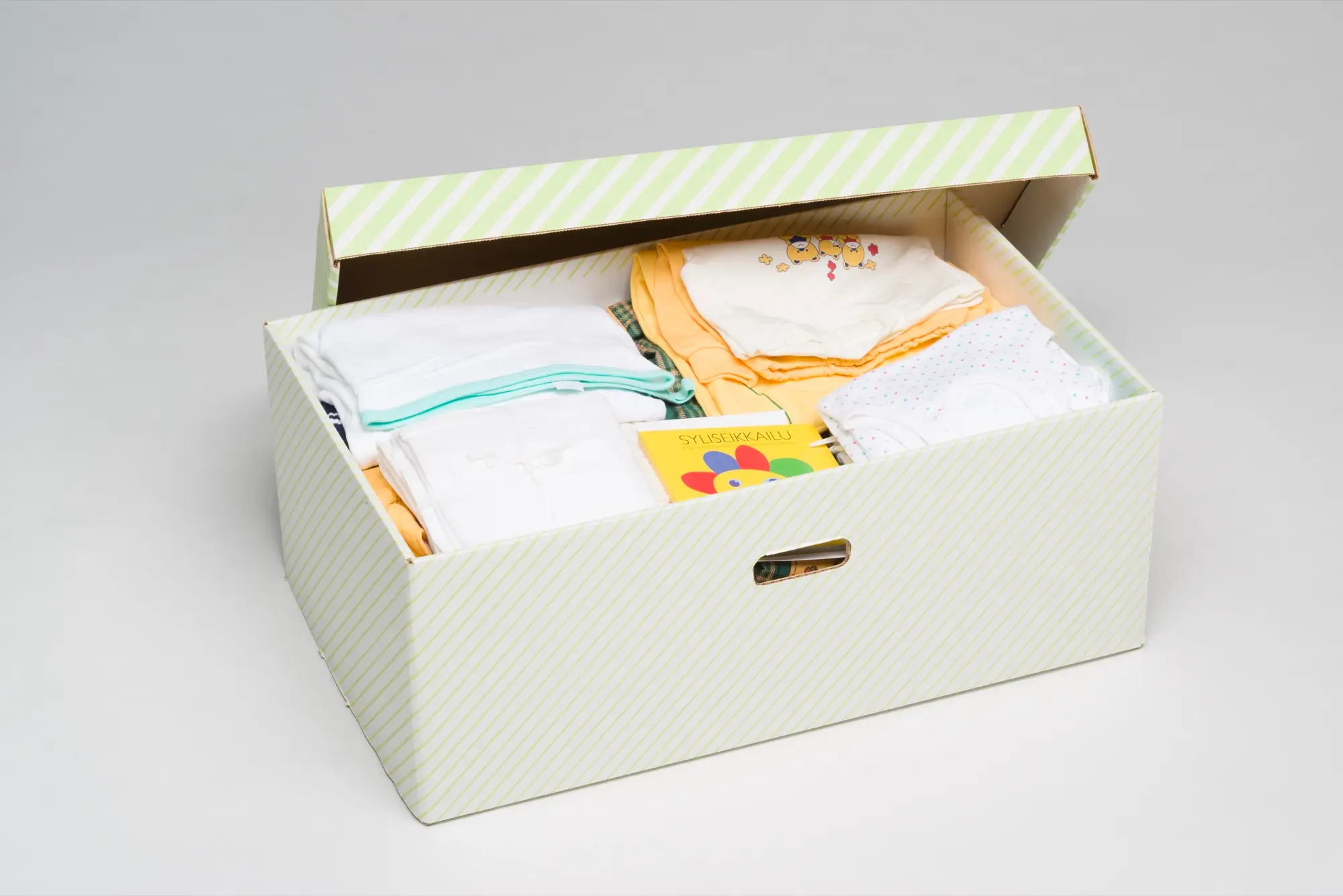 An open Finnish maternity package box filled with folded baby clothes and a picture book.