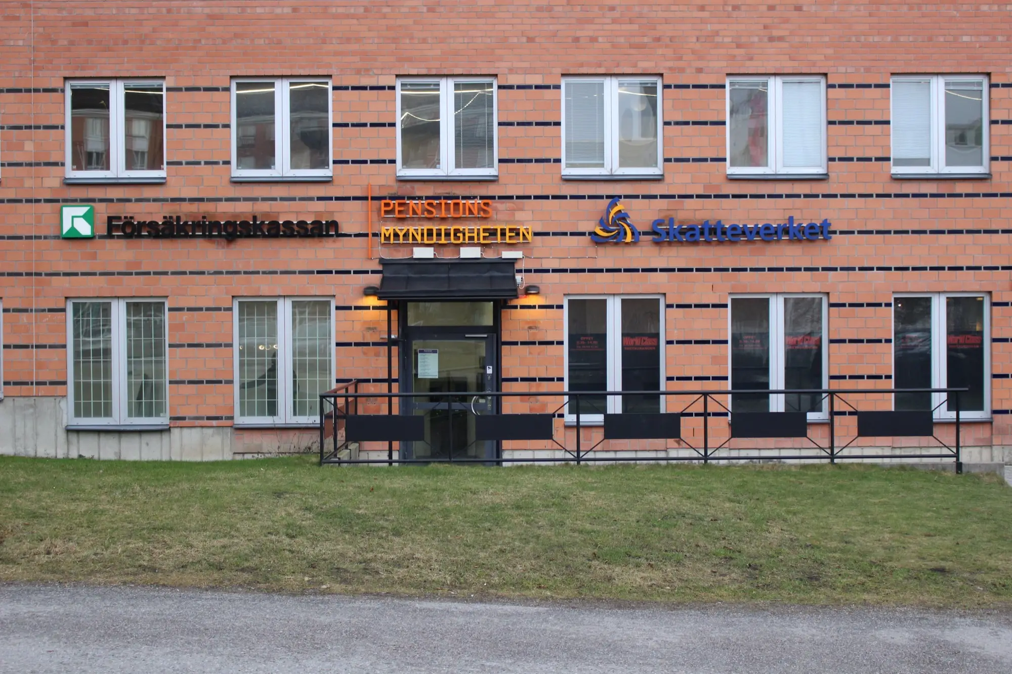 A red-brick office building in Kista, Stockholm, with the signs of Försäkringskassan, Pensionsmyndigheten and Skatteverket above its entrance.