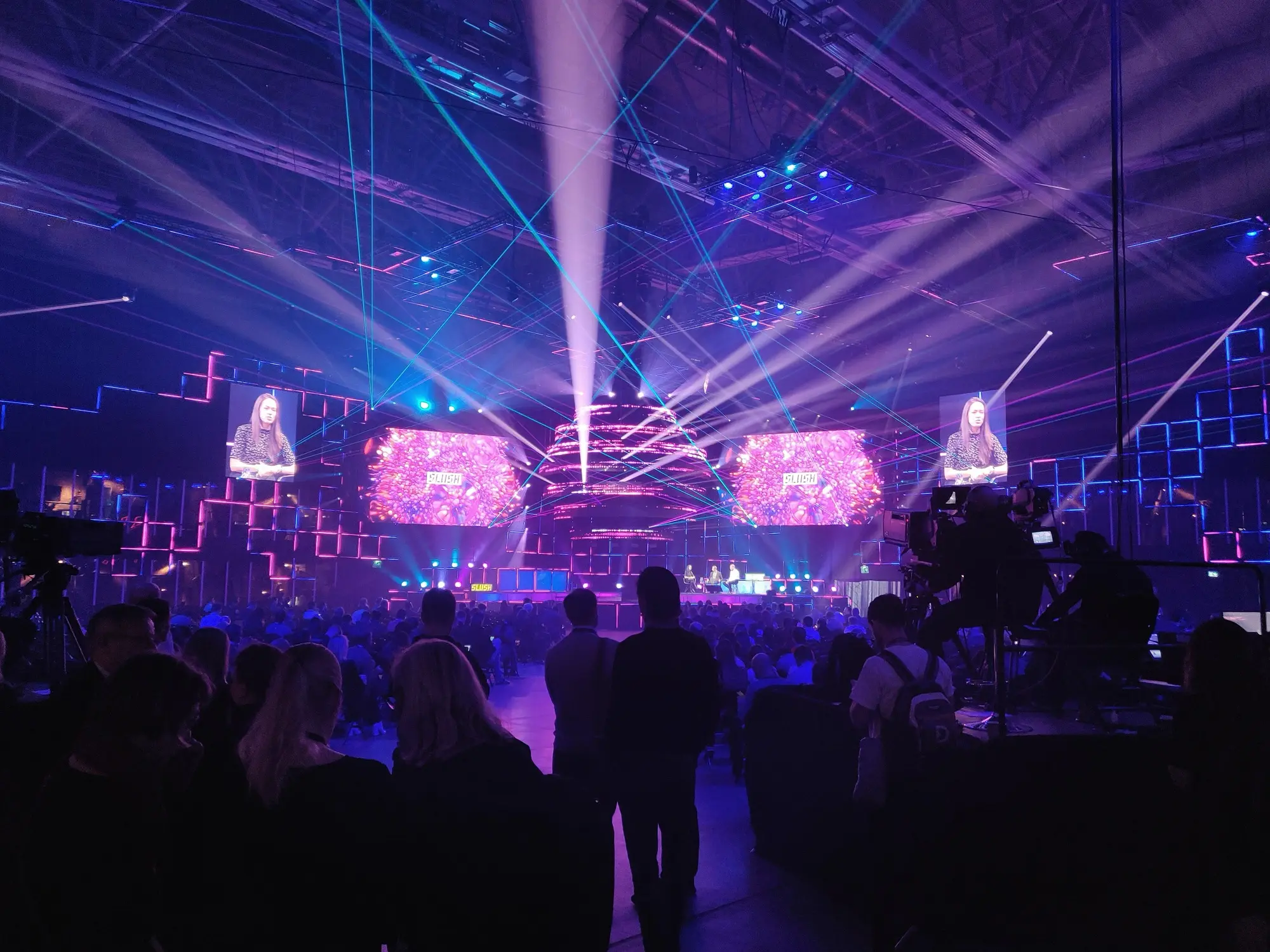 A crowd watches a stage lit with purple and blue laser beams at the Slush startup event in Helsinki.