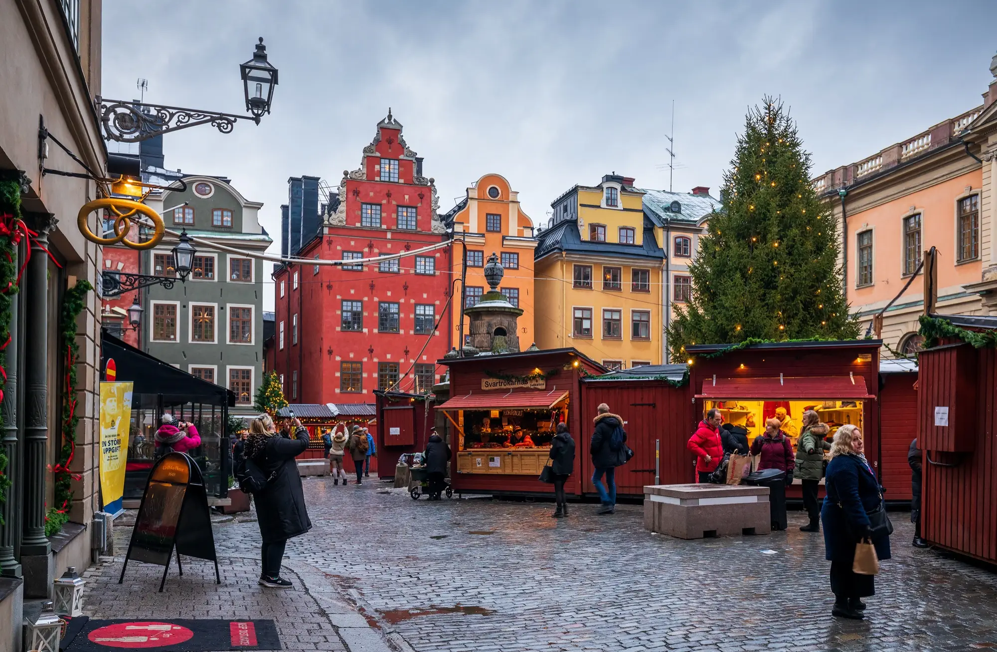 The Christmas market on Stortorget in Gamla stan, Stockholm, in December: red wooden stalls, a lit Christmas tree and the square's red and yellow gabled houses.