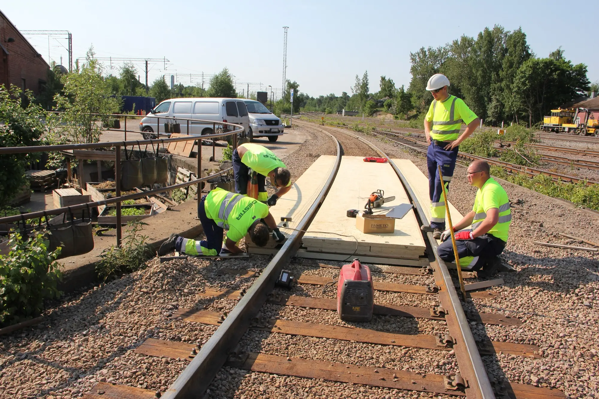 Workers in high-visibility clothing repairing railway track in a Finnish rail yard on a sunny day.
