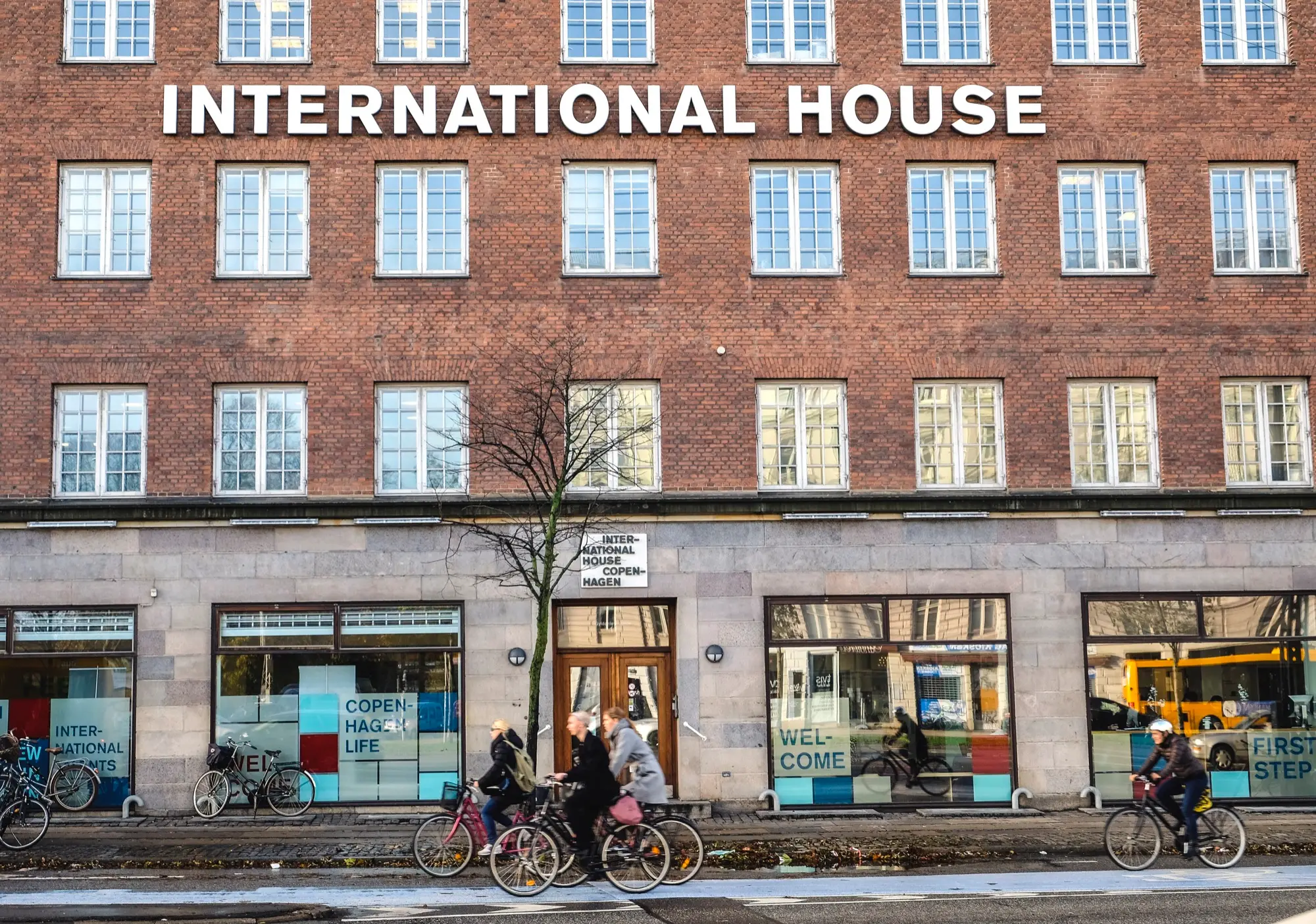 Cyclists passing the red-brick front of International House Copenhagen, where newcomers register and SIRI has a service desk
